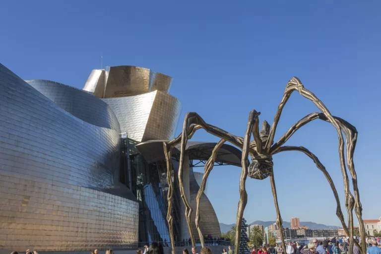 Bilbao, Spania - 29. oktober 2016; baksiden av Guggenheim-museet, samtidskunst, verk av den kanadiske arkitekten Frank O. Gehry og skulpturen av edderkoppen til Louise Bourgeois. Det er mennesker som går