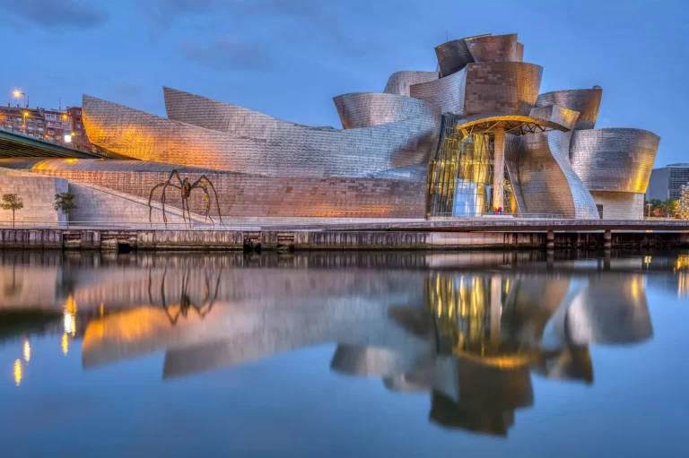 Bilbao, Spanje - 10 juli 2021: Het beroemde Guggenheim Museum weerspiegeld in de rivier de Nervion bij zonsopgang