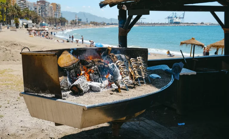 Primo piano di alcuni espetos, una sorta di spiedini in cui il pesce viene infilzato per essere cucinato sul fuoco a legna, un metodo di cottura tradizionale di Malaga, nella spiaggia di La Malagueta, a Malaga, in Spagna.