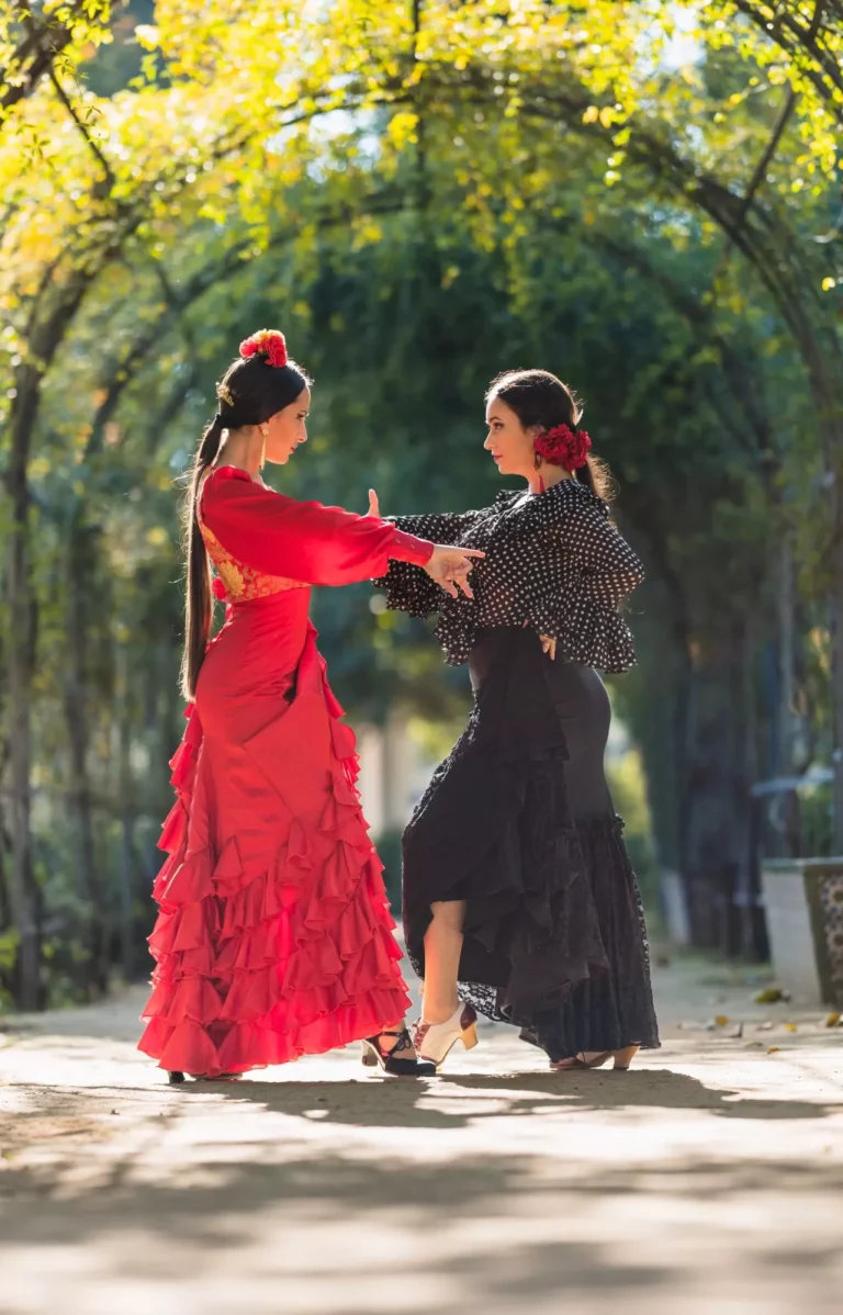 Vertical photo of two women in flamenco dresses dancing together in a garden with an arch of plants