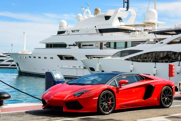 Marbella, Spanien - 13. Oktober 2016: Frontansicht eines roten Supersportwagens (Lamborghini), der neben Luxusjachten geparkt ist, die im Yachthafen von Puerto Jose Banus an der Costa del Sol in Marbella, Spanien, festgemacht sind.