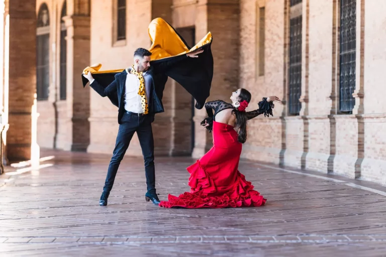 Hombre y mujer con traje de flamenca bailando a la sombra de la Plaza de España de Sevilla